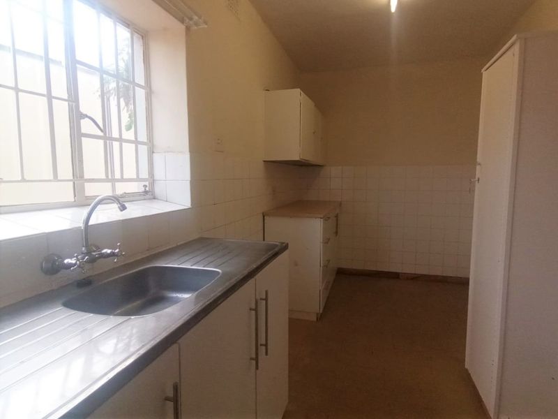 A functional, empty kitchen featuring built-in cabinetry, a stainless steel sink, and tiled splashbacks, offering a blank canvas for renovation.