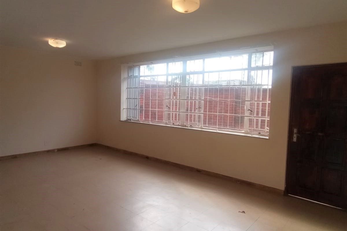An empty, neutrally painted living area featuring tiled flooring, security bars on the windows, and two flush-mount ceiling lights.