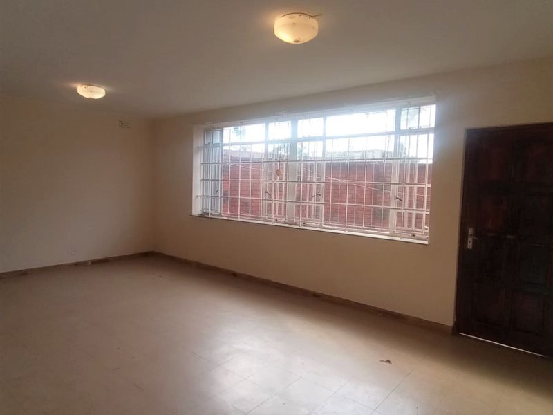 An empty, neutrally painted living area featuring tiled flooring, security bars on the windows, and two flush-mount ceiling lights.