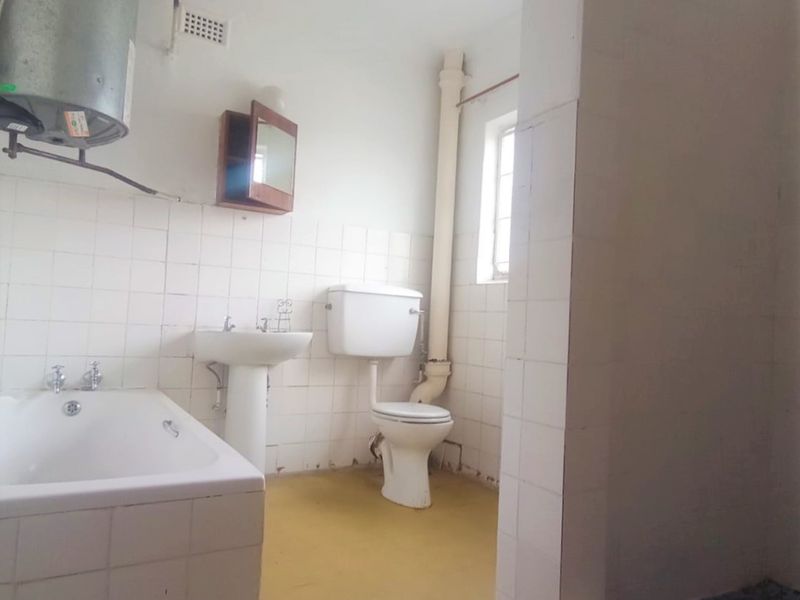 A dated bathroom featuring a bathtub, pedestal basin, toilet, and separate shower enclosure, requiring modernization of finishes and fixtures.