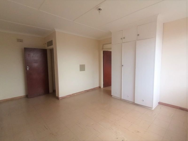 An empty bedroom featuring built-in cupboards, tiled flooring, and coved ceilings, offering a blank canvas for renovation or interior design updates.