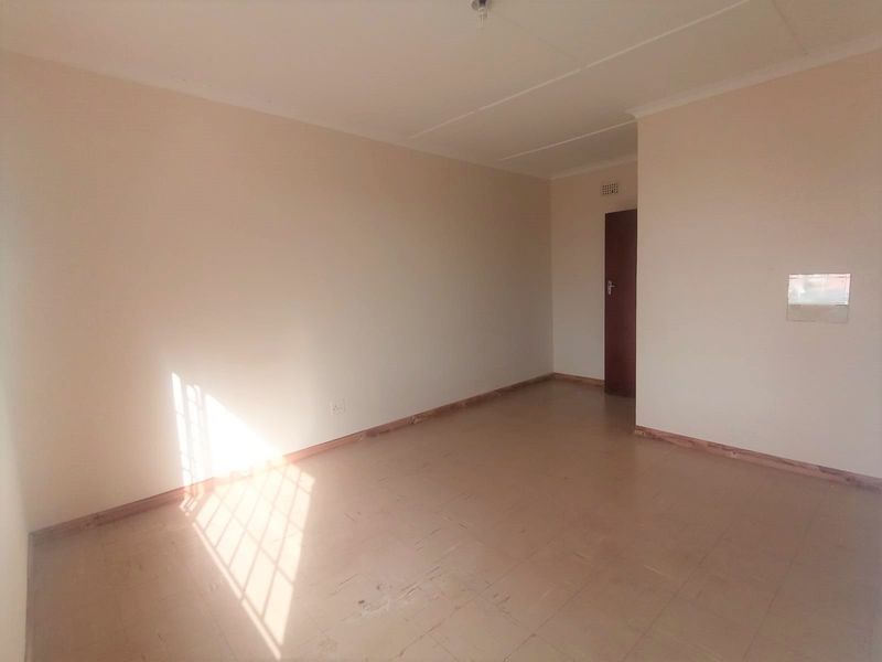 A vacant, neutrally painted living area featuring tiled flooring and simple architectural finishes, offering a blank canvas for potential interior design updates.