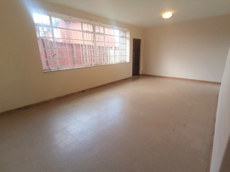 A spacious, empty living area featuring large steel-framed windows, neutral walls, and tiled flooring, offering a blank canvas for interior design.