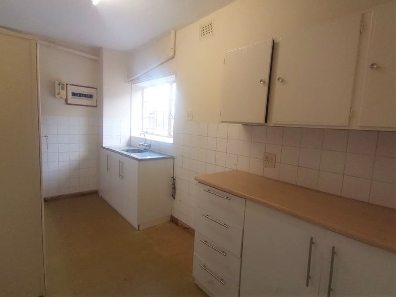 A functional, empty kitchen featuring white built-in cabinetry, laminate countertops, a stainless steel sink, and tiled splashbacks, offering potential for modern renovation.