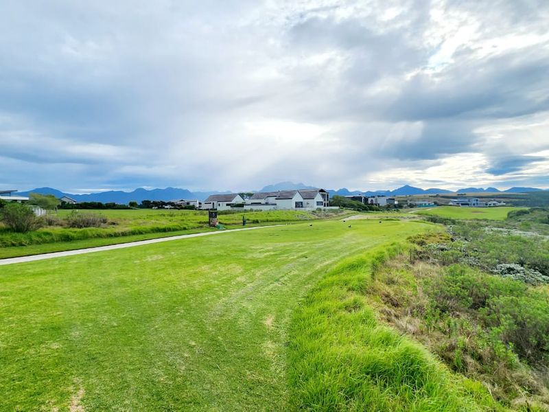 A scenic view of a well-maintained residential estate featuring expansive green lawns, paved pathways, and distant mountain vistas under a cloudy sky.