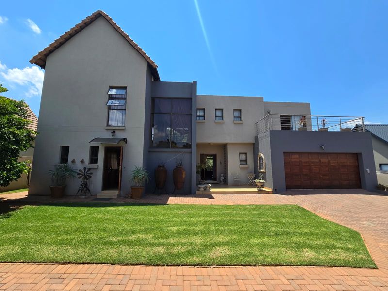 A modern double-story residential property featuring a paved driveway, double garage, and a balcony with metal balustrades under a clear blue sky.