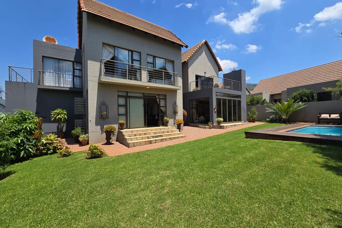 Rear view of a double-story house featuring a landscaped garden, swimming pool with wooden decking, and upper-level balconies.