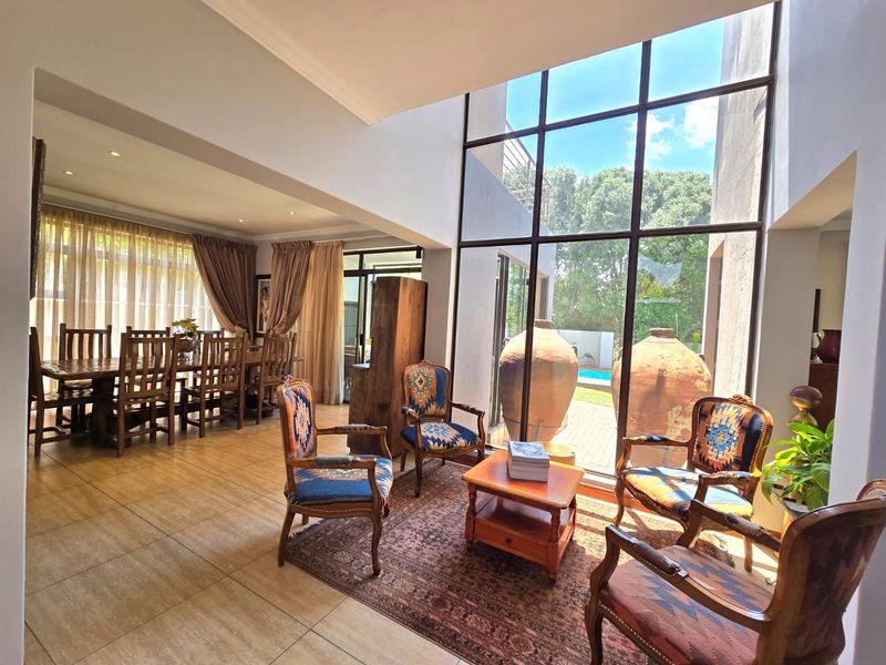 Spacious open-plan living and dining area featuring double-volume floor-to-ceiling windows that provide abundant natural light and views of the garden and pool.