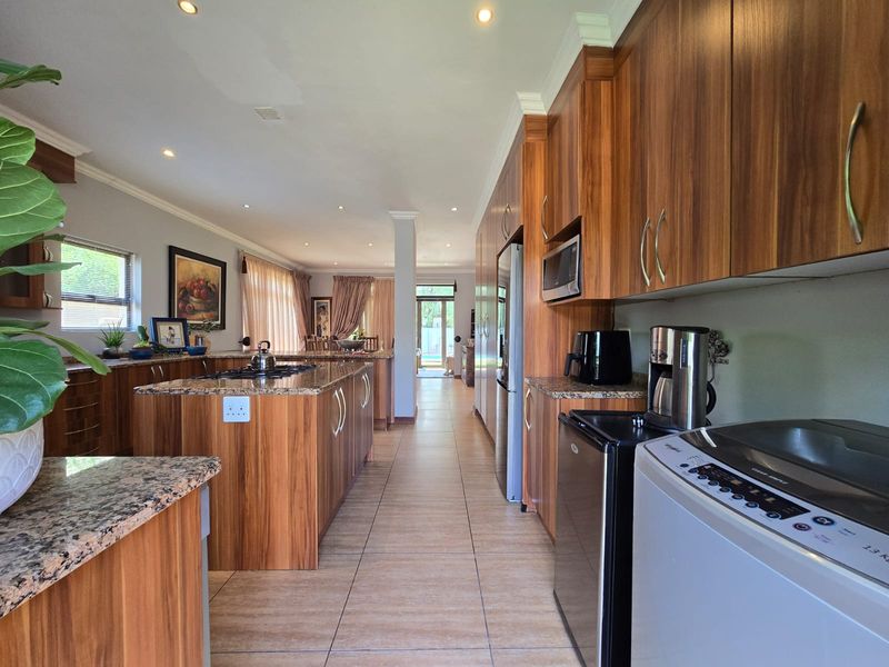 Spacious open-plan kitchen featuring wood veneer cabinetry, granite countertops, and integrated appliances, flowing seamlessly into the dining and living areas.
