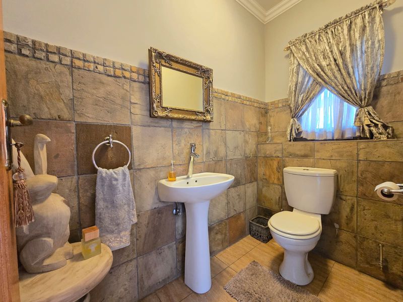 A compact bathroom featuring stone-tiled walls, a white pedestal basin, and a standard ceramic toilet.