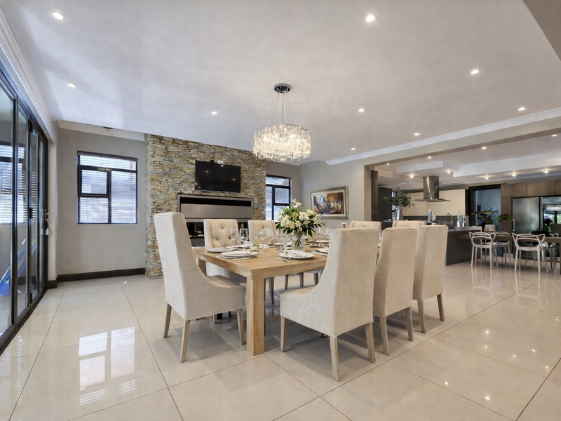 Spacious open-plan dining and kitchen area featuring polished porcelain tiles, a striking stone-clad fireplace, and modern recessed lighting throughout.