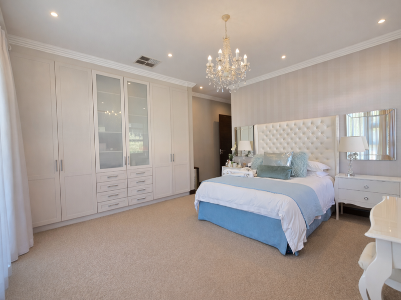 A well-appointed bedroom featuring extensive built-in cabinetry, neutral carpeting, crown molding, and recessed lighting, creating a polished and comfortable living space.