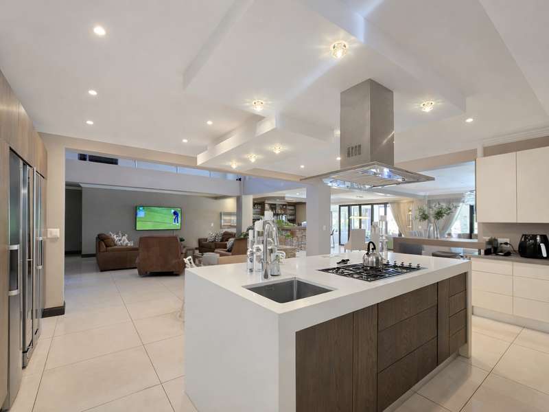 Modern open-plan kitchen featuring a central island with gas cooktop, stainless steel extractor, and sleek cabinetry, seamlessly flowing into the living area.
