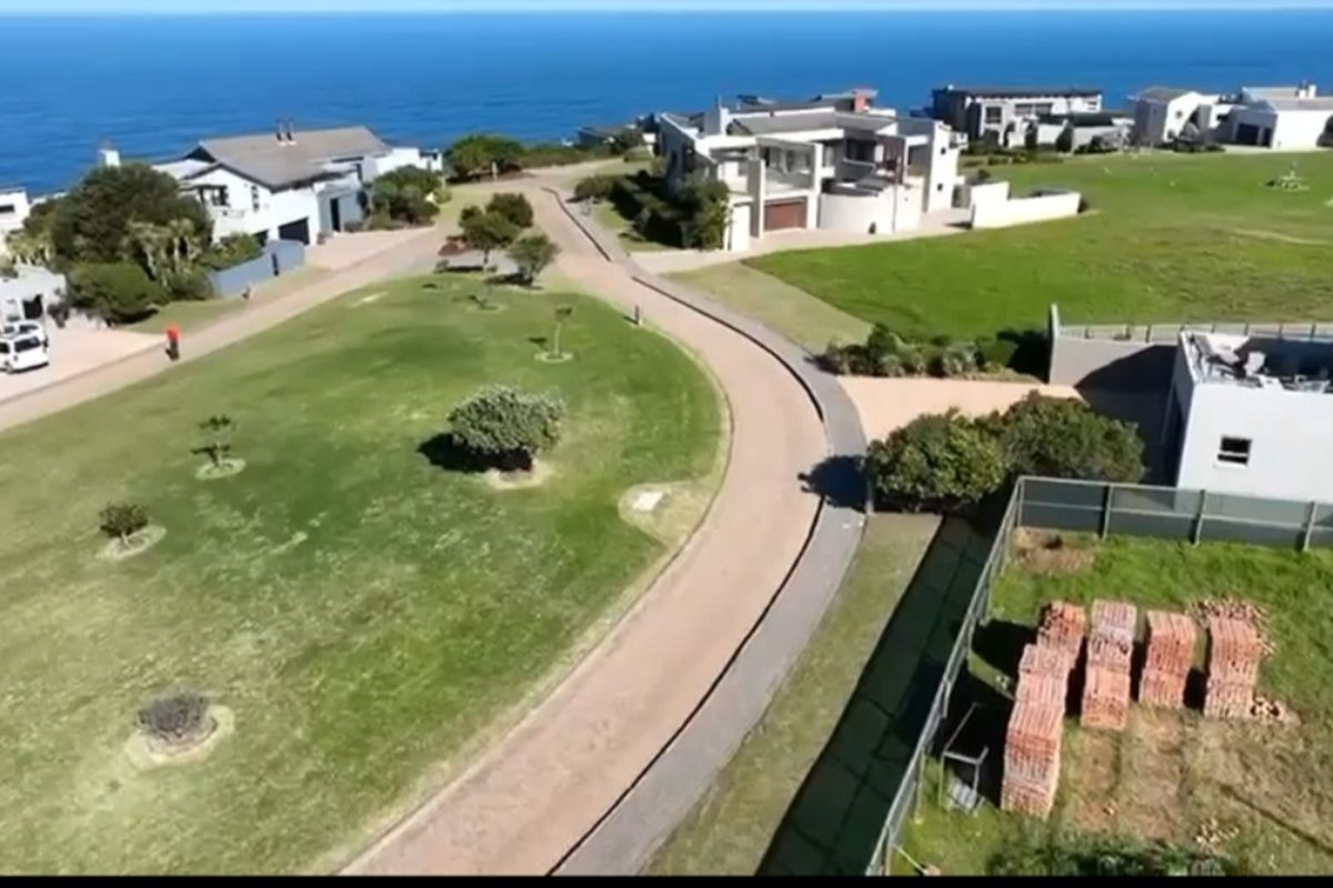 An aerial view of a coastal residential estate featuring paved roads, manicured lawns, and surrounding modern homes with ocean views.