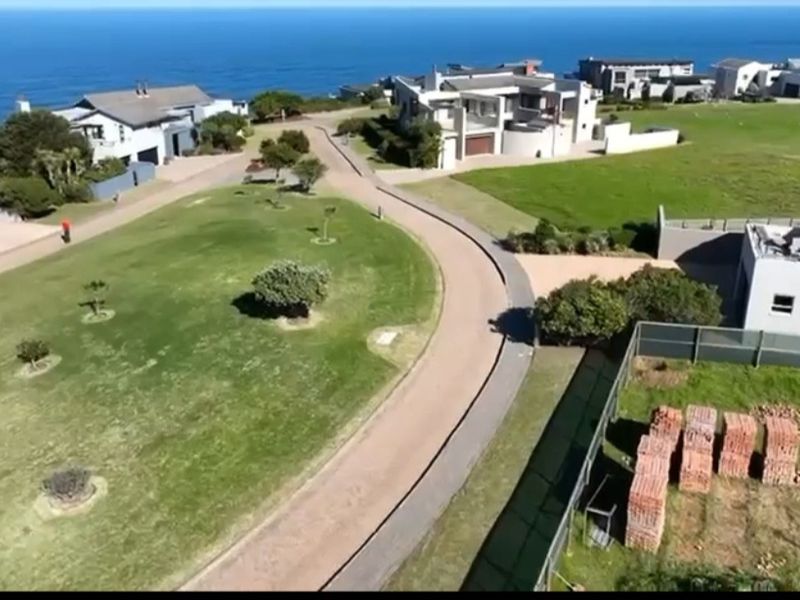An aerial view of a coastal residential estate featuring paved roads, manicured lawns, and surrounding modern homes with ocean views.
