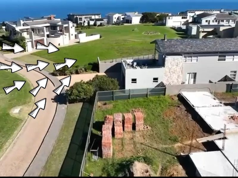 Aerial view of a residential estate showing surrounding properties, paved access roads, and an active construction site with building materials.