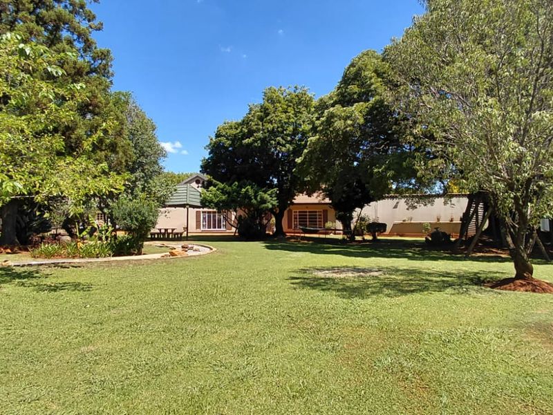 A spacious, well-maintained garden featuring mature trees, a manicured lawn, and a paved pathway leading toward the rear of the property.