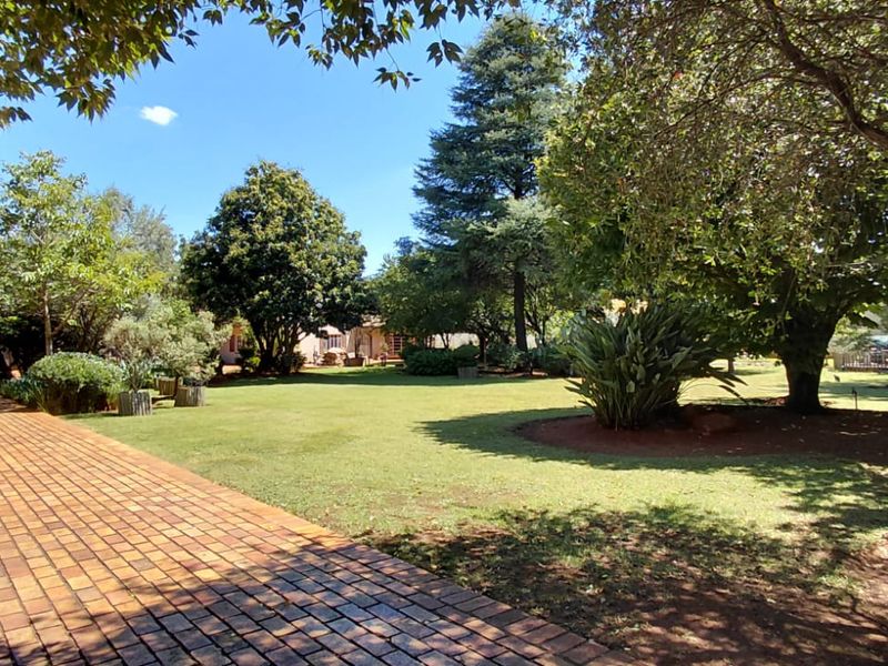 A spacious, well-maintained garden featuring a brick-paved driveway, expansive lawn, and mature trees providing a serene outdoor setting.