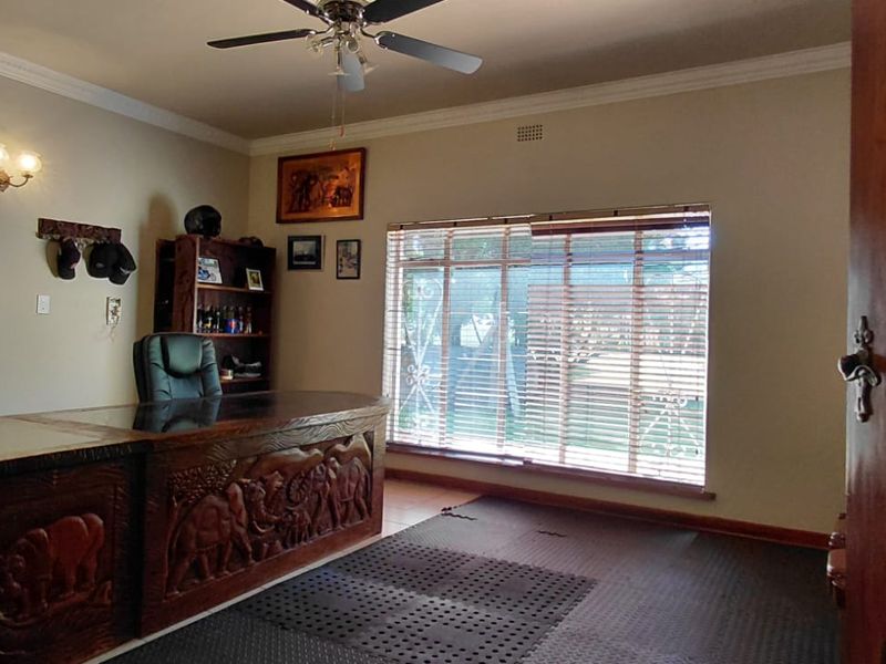 A functional home office space featuring crown molding, a ceiling fan, and large windows with venetian blinds and security gates.