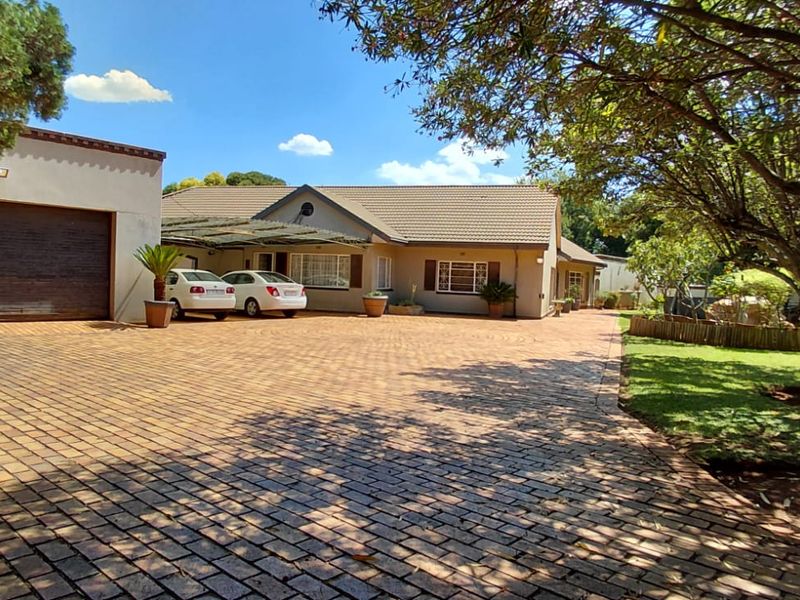 Front view of a residential property featuring a spacious paved driveway, attached garage, carport, and well-maintained garden area.