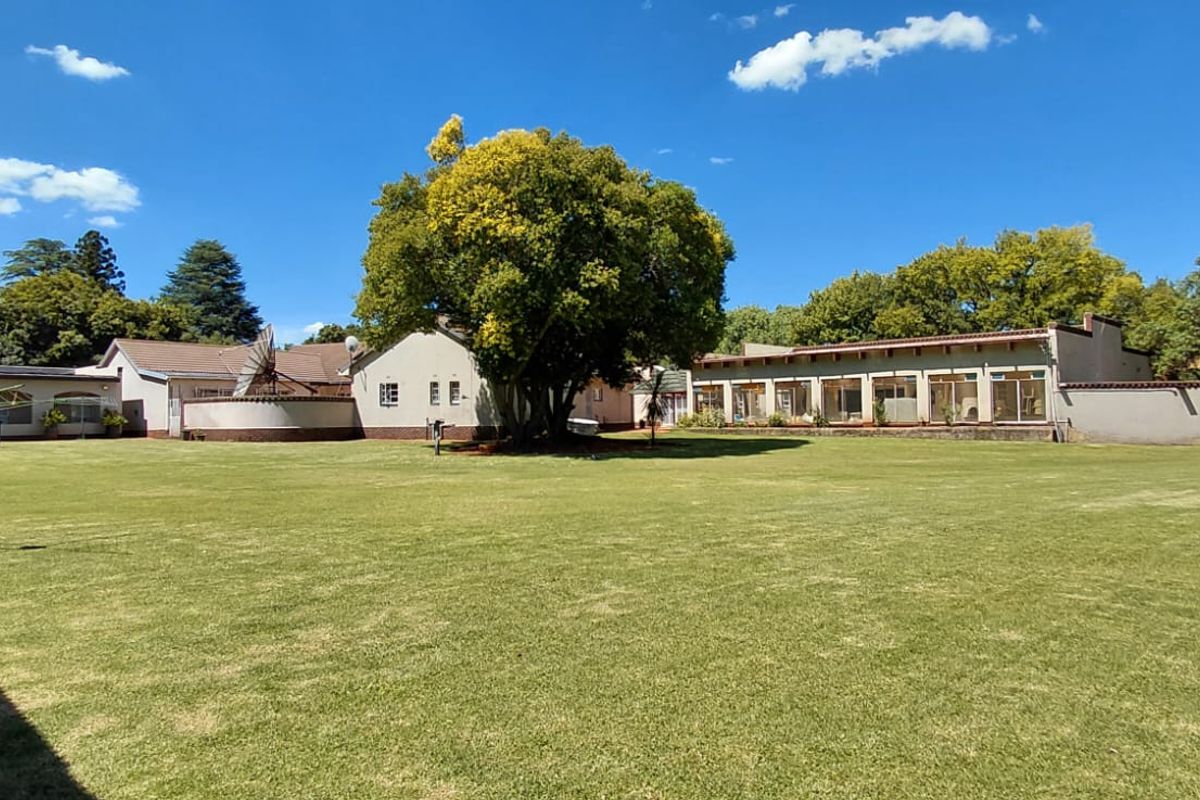 Spacious rear garden featuring a large manicured lawn, mature trees, and a view of the property's rear facade with extensive glass sliding doors.