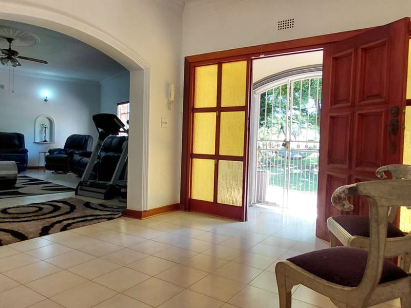 Welcoming entrance hall featuring tiled flooring, an arched transition to the living area, and a timber-framed glass door with an integrated security gate.