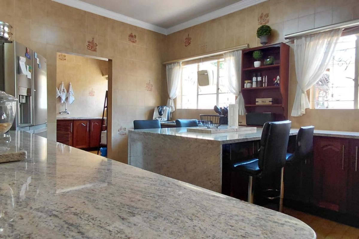 A functional kitchen featuring granite countertops, a central island, and tiled wall finishes, with an adjacent scullery area visible.