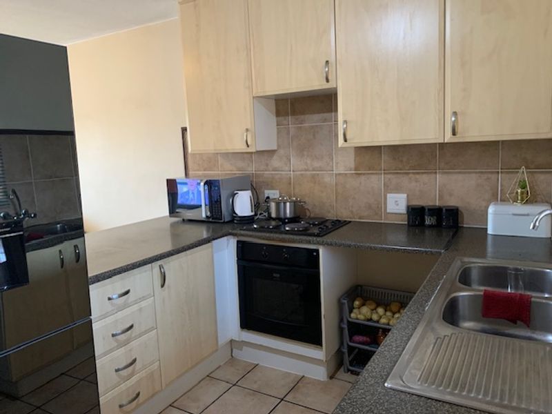 A functional kitchen featuring light wood-tone cabinetry, dark laminate countertops, a built-in oven with electric hob, and a double stainless steel sink.