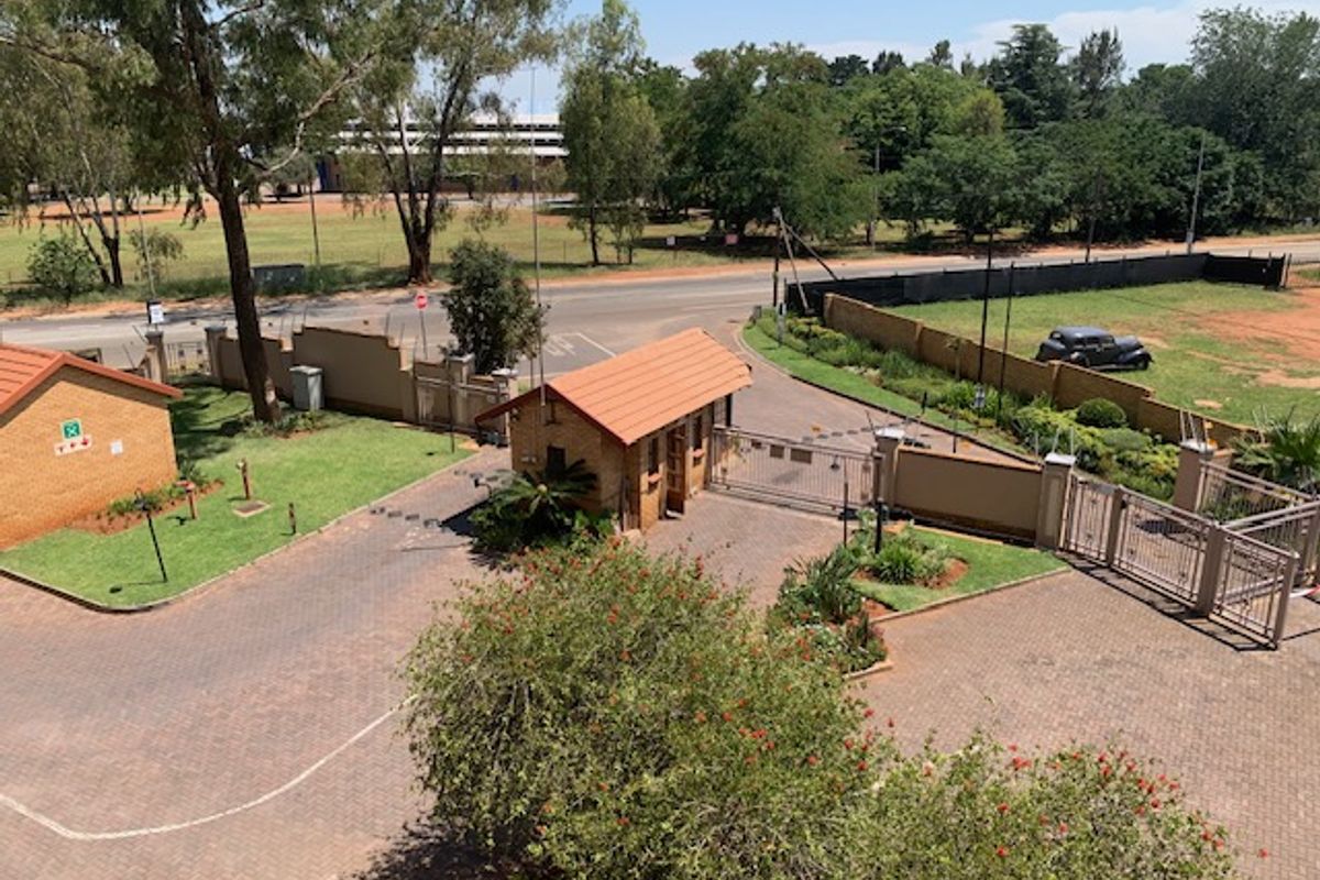 Aerial view of the apartment complex entrance featuring a security gatehouse, paved driveway, and perimeter wall with automated access control.