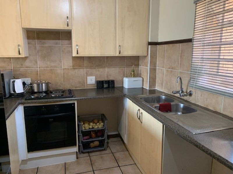 A functional kitchen featuring light wood-finish cabinetry, tiled backsplash, built-in oven and hob, and a double stainless steel sink with tiled flooring.