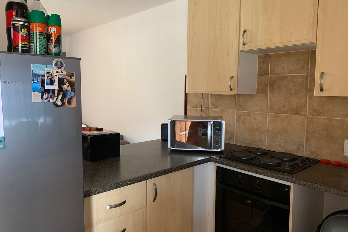 Compact kitchen featuring light wood-finish cabinetry, dark laminate countertops, tiled backsplash, and integrated electric cooking appliances.