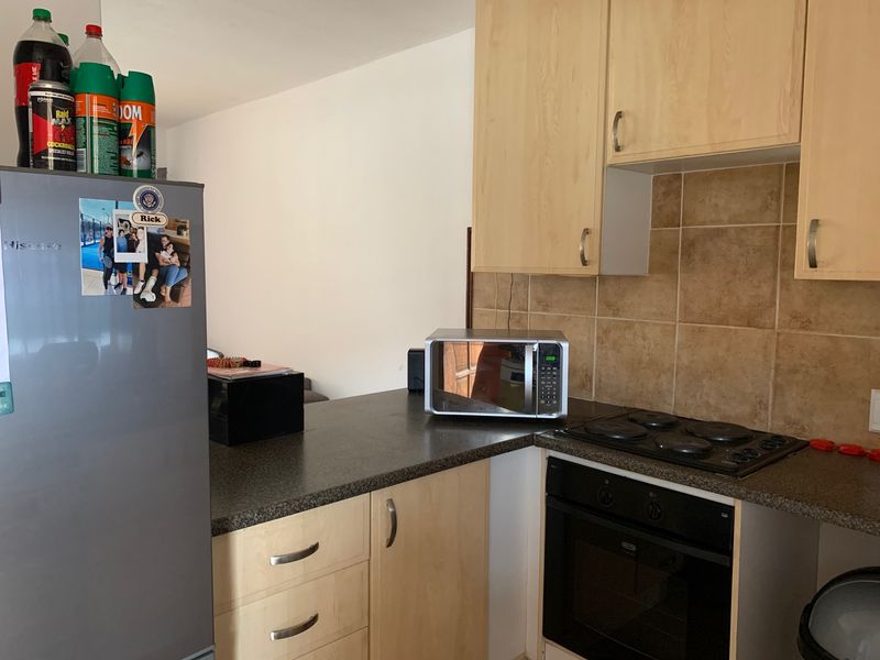 Compact kitchen featuring light wood-finish cabinetry, dark laminate countertops, tiled backsplash, and integrated electric cooking appliances.