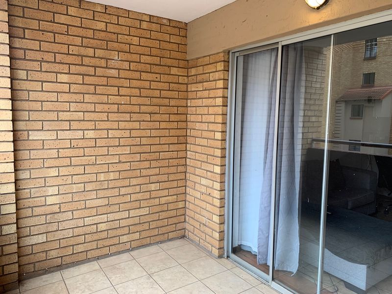 A covered balcony featuring exposed brick walls, tiled flooring, and a large sliding glass door providing access to the interior living space.
