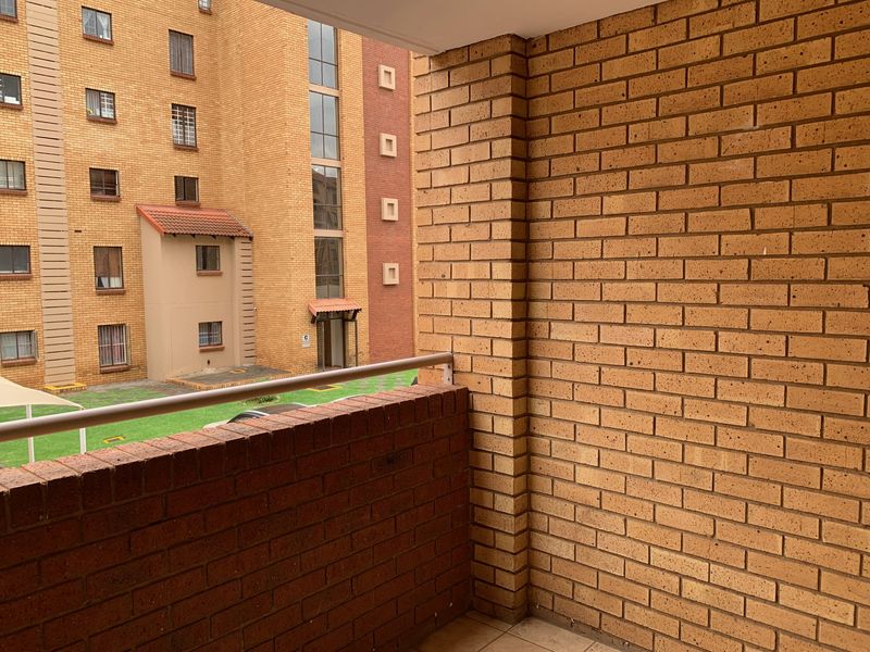 A private balcony featuring brick walls and a metal railing, overlooking the apartment complex courtyard.