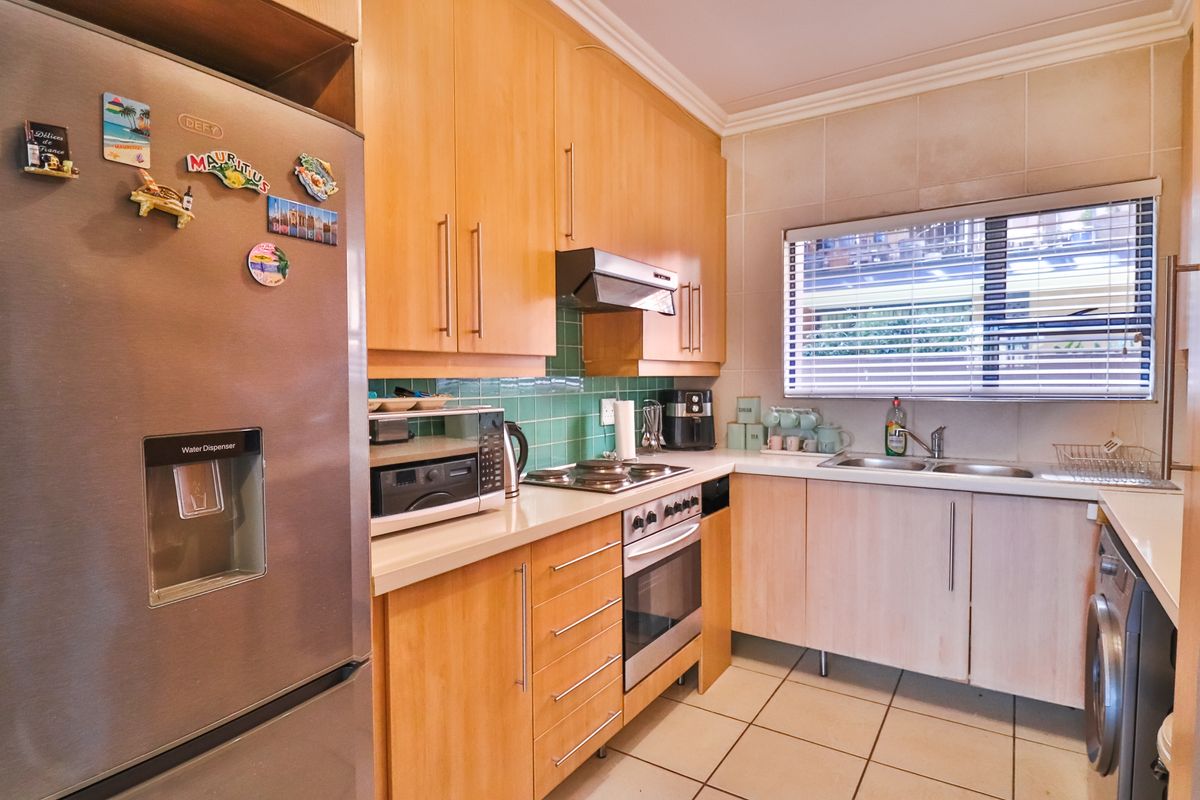 A functional kitchen featuring light wood cabinetry, tiled backsplash, stainless steel oven, electric hob, and a double bowl sink with window views.