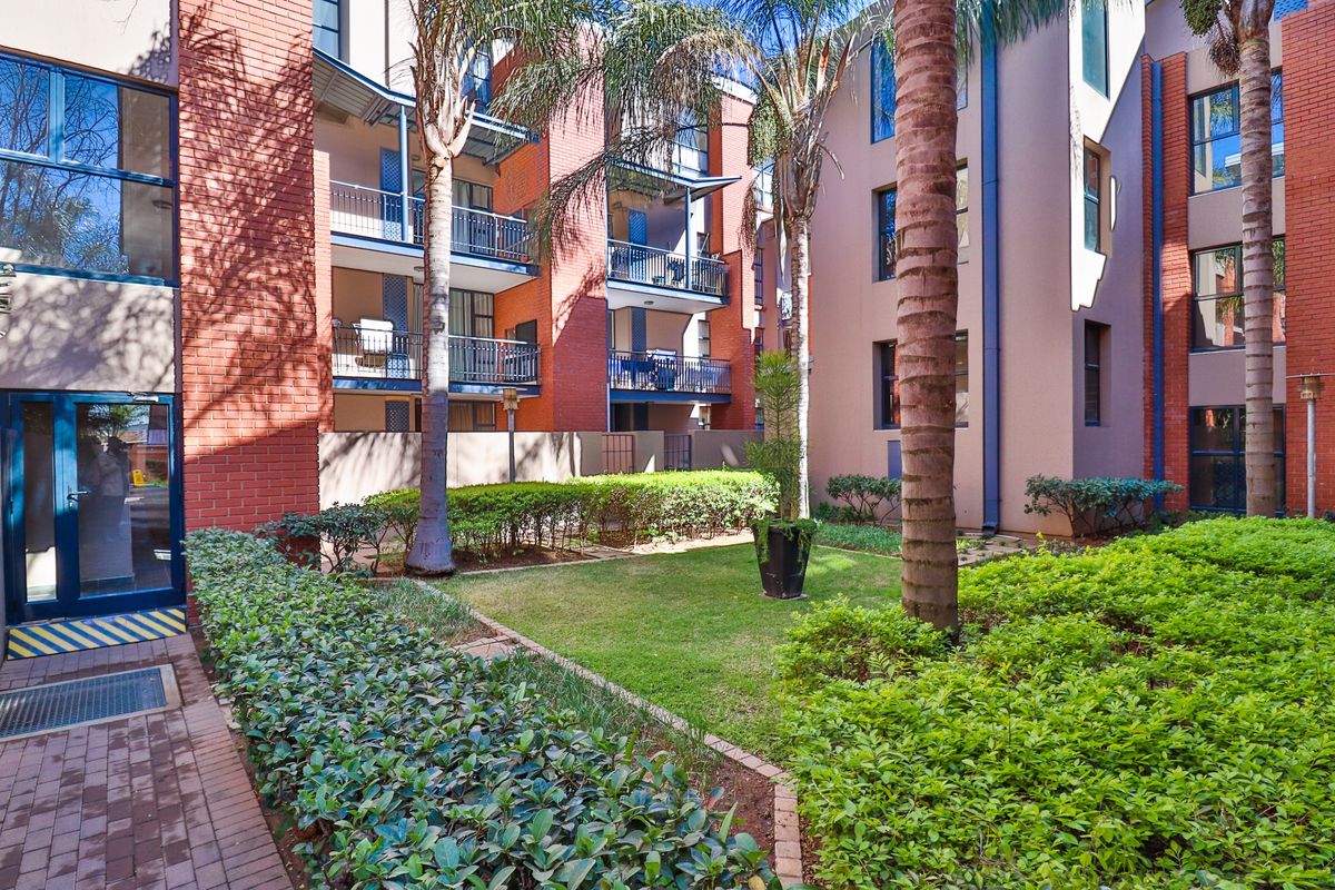 A well-maintained apartment complex courtyard featuring a landscaped garden, paved pathways, and multi-story brick facade with private balconies.