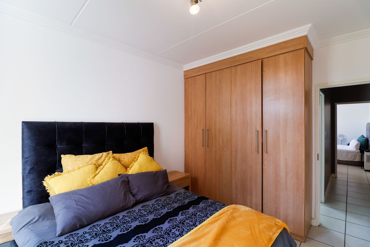 A well-maintained bedroom featuring a large built-in wooden wardrobe, tiled flooring, and decorative ceiling coving.