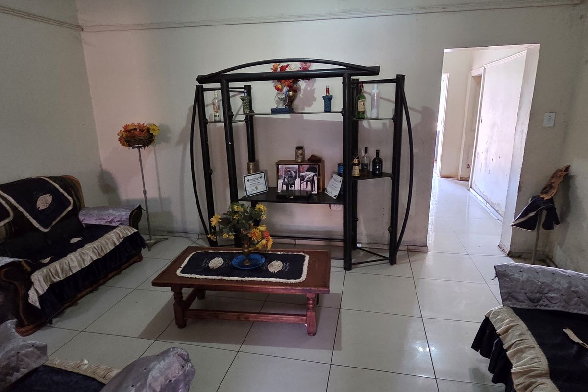 A living room featuring tiled flooring and coving, currently showing signs of wear including peeling paint and wall surface damage.