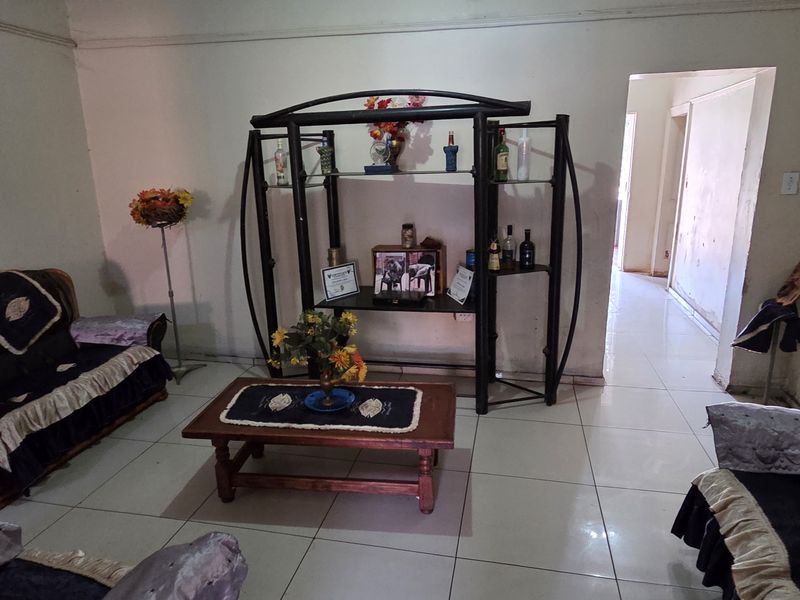 A living room featuring tiled flooring and coving, currently showing signs of wear including peeling paint and wall surface damage.