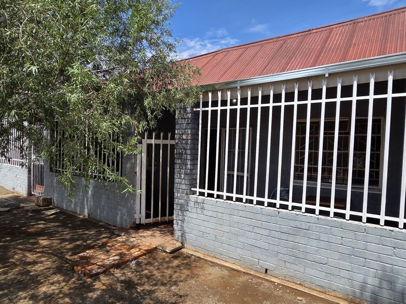 Front exterior view of a house featuring painted brick walls, a corrugated metal roof, and security bars installed on windows and the entrance.