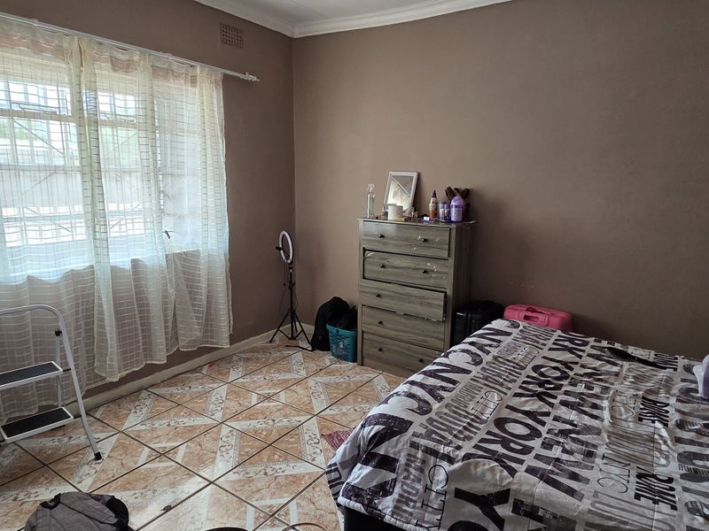 A bedroom featuring tiled flooring, a window with security bars, and a built-in cupboard, requiring cosmetic updates to improve its overall condition.