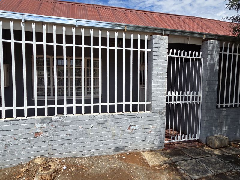 Front exterior view of a brick house featuring a corrugated metal roof and comprehensive security fencing and gate.