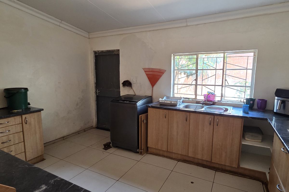 A functional kitchen space featuring laminate cabinetry, a double bowl sink, and tiled flooring, currently showing signs of wear and wall staining.