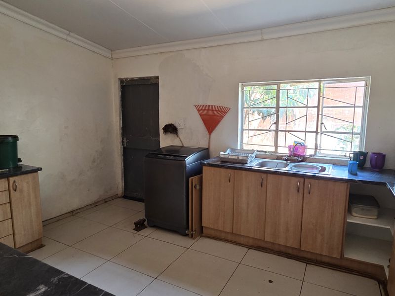 A functional kitchen space featuring laminate cabinetry, a double bowl sink, and tiled flooring, currently showing signs of wear and wall staining.