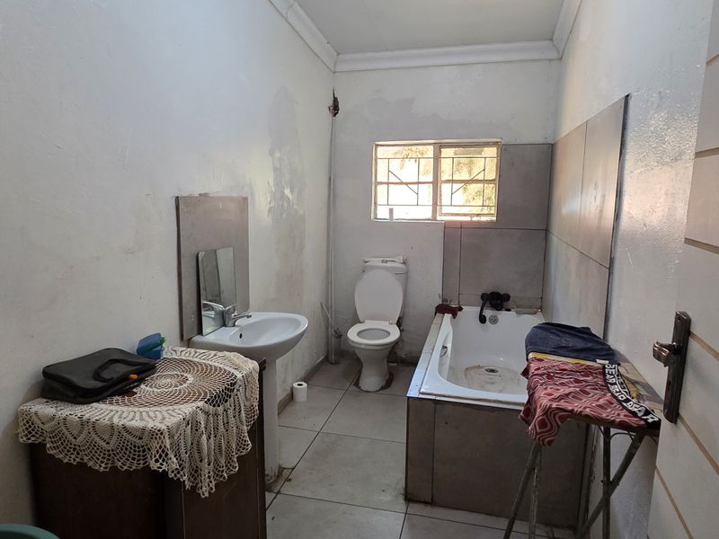 A dated bathroom featuring a pedestal basin, toilet, and built-in bathtub with tiled splashbacks, requiring cosmetic updates and wall repairs.