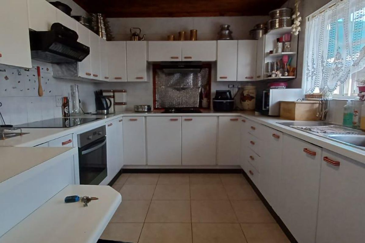 A functional U-shaped kitchen featuring white cabinetry, tiled flooring, a built-in oven, and a double-basin sink with a window view.