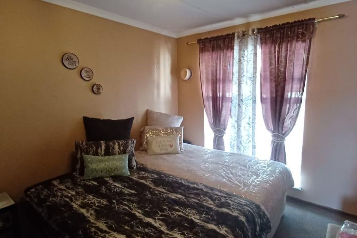 A bedroom featuring neutral wall tones, carpeted flooring, and a window dressed with layered curtains.