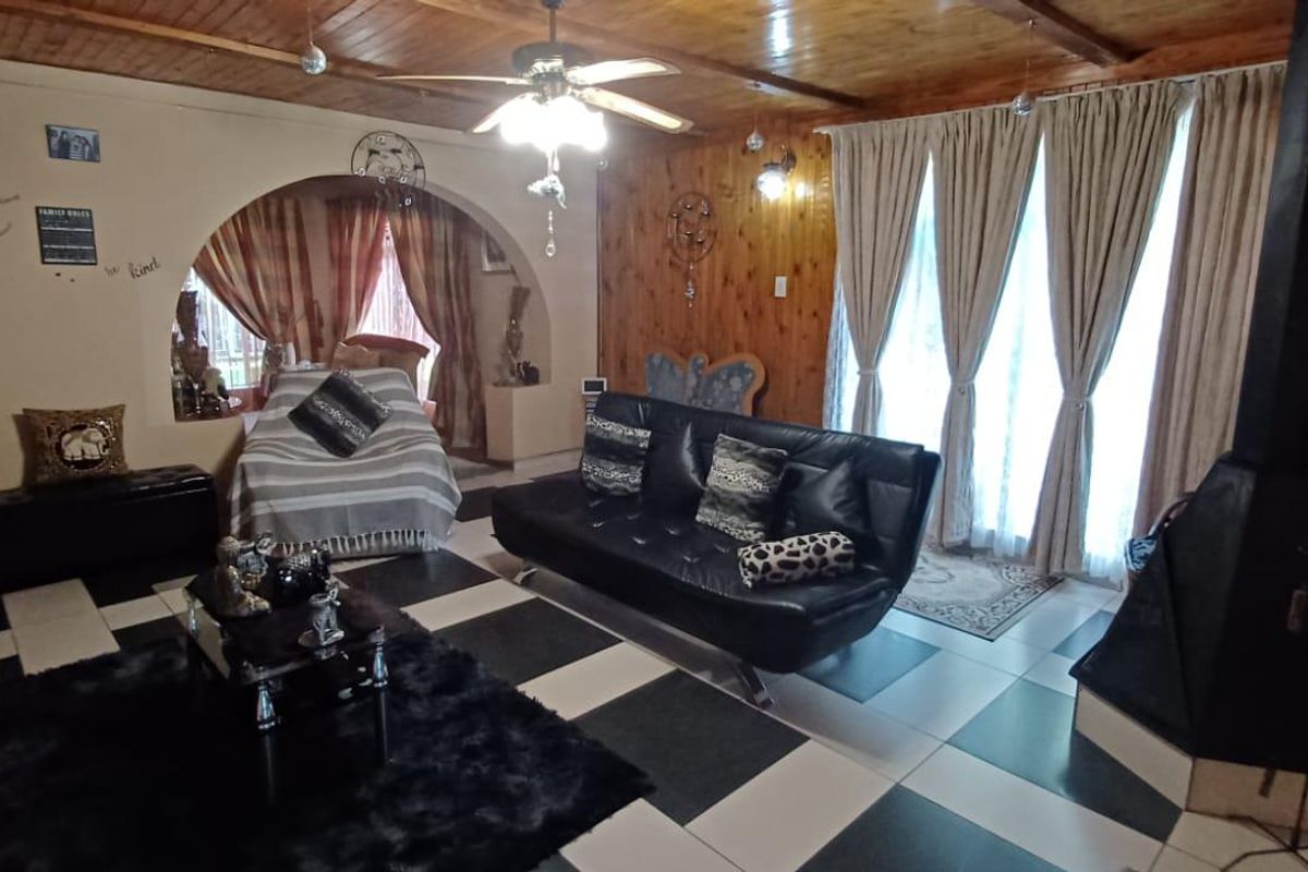 Spacious living room featuring a built-in fireplace, wood-paneled ceiling, and large windows with access to an adjoining room through an arched doorway.