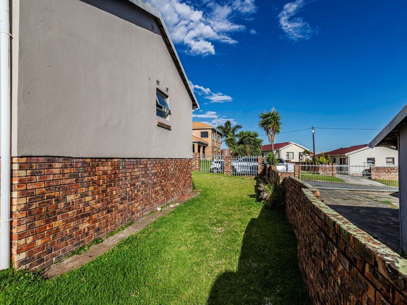 A side view of the property showing a grassed area, brick boundary wall, and metal gate access to the driveway.