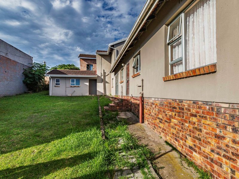 Rear view of the property featuring a brick and plaster facade, tiled roof, and a spacious backyard area with a paved walkway.